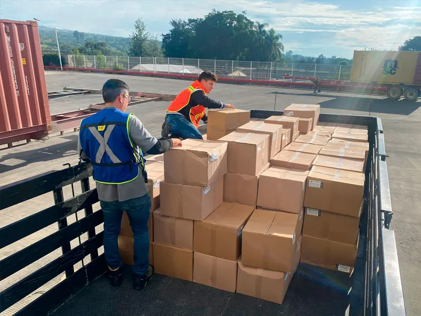 Personal con chaleco cargando cajas en un andén