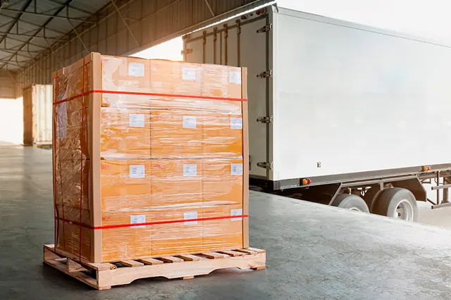 Tarima de cajas estibadas y emplayadas frente a la caja del camión